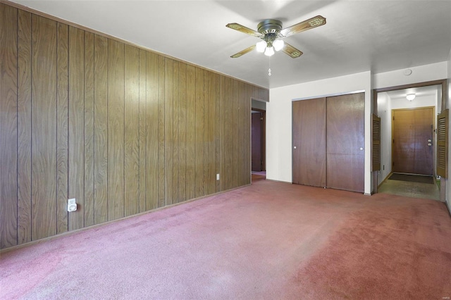 unfurnished bedroom with ceiling fan, light colored carpet, and wooden walls