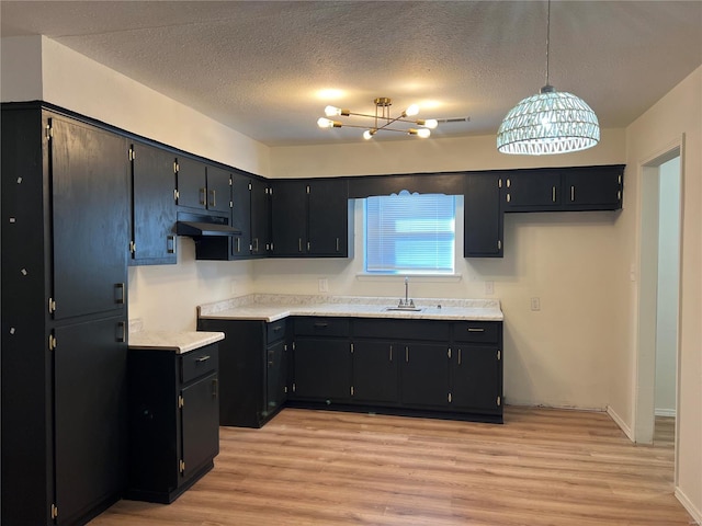 kitchen featuring light wood-type flooring, hanging light fixtures, a notable chandelier, and sink