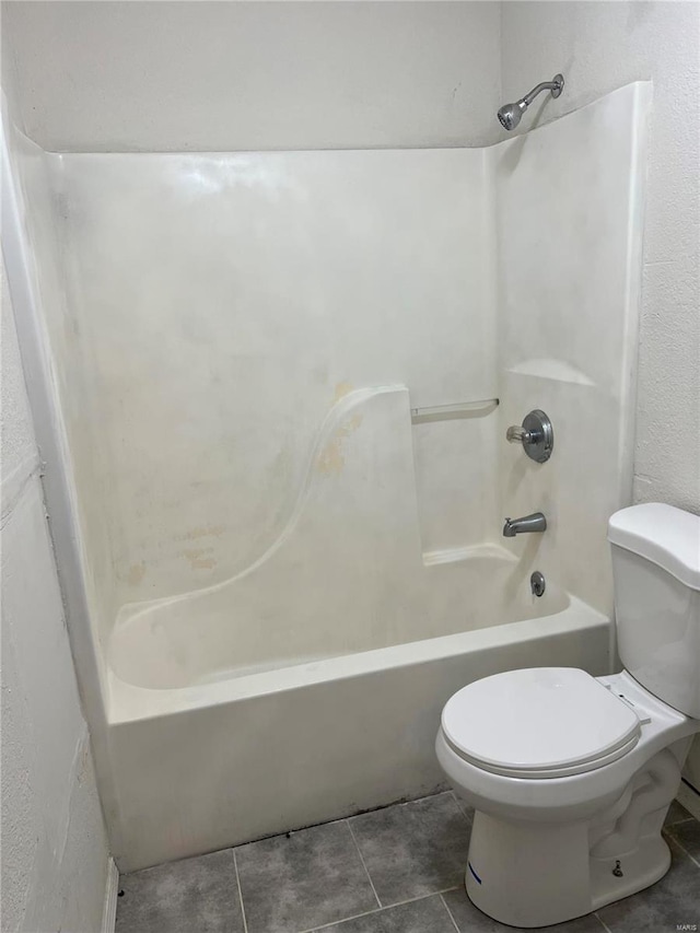 bathroom featuring tile patterned flooring, washtub / shower combination, and toilet