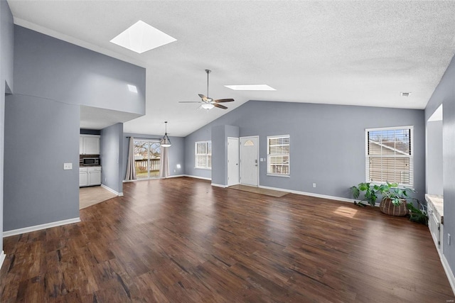 unfurnished living room featuring ceiling fan, plenty of natural light, dark hardwood / wood-style floors, and vaulted ceiling with skylight