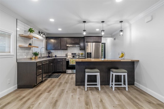 kitchen featuring sink, stainless steel appliances, crown molding, light hardwood / wood-style floors, and a kitchen bar