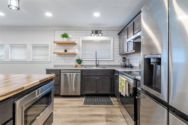 kitchen with sink, stainless steel appliances, tasteful backsplash, range hood, and light wood-type flooring