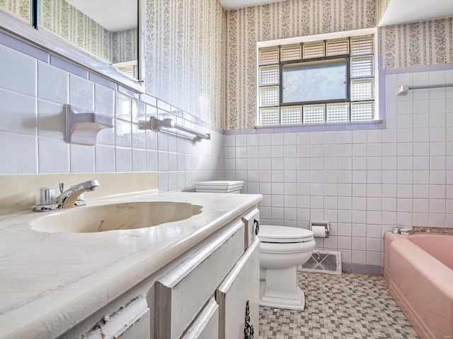 bathroom with a bathtub, vanity, tile patterned floors, toilet, and tile walls