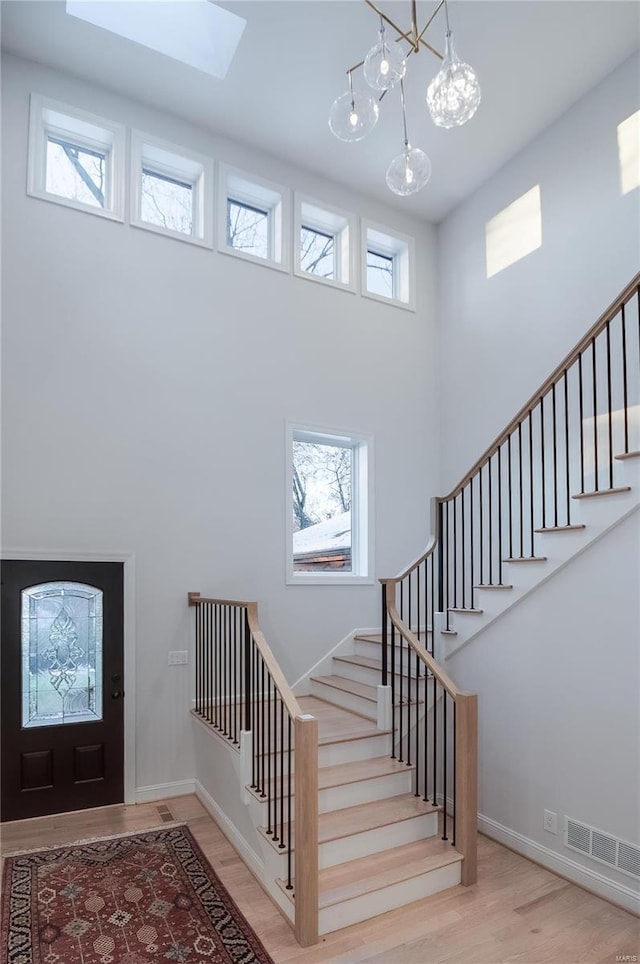 foyer entrance featuring an inviting chandelier, a high ceiling, a wealth of natural light, and light hardwood / wood-style flooring