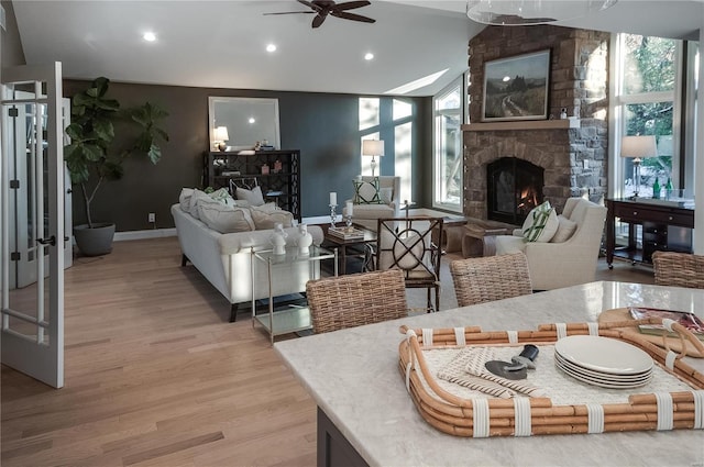 living room with light hardwood / wood-style floors, a stone fireplace, a wealth of natural light, and lofted ceiling