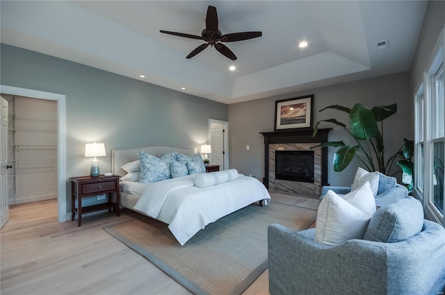 bedroom featuring ceiling fan, a spacious closet, light hardwood / wood-style flooring, a fireplace, and a closet