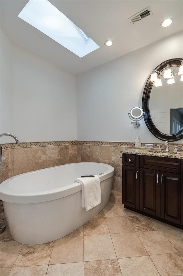 bathroom with a skylight, tile patterned flooring, a tub to relax in, vanity, and tile walls