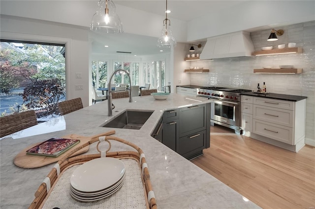 kitchen with pendant lighting, custom exhaust hood, range with two ovens, light hardwood / wood-style flooring, and dark stone countertops