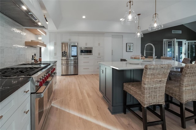 kitchen with white cabinets, wall chimney exhaust hood, lofted ceiling, and appliances with stainless steel finishes