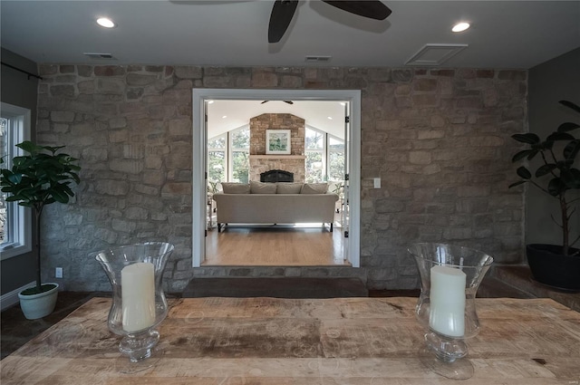 living room with hardwood / wood-style floors, a stone fireplace, ceiling fan, and lofted ceiling