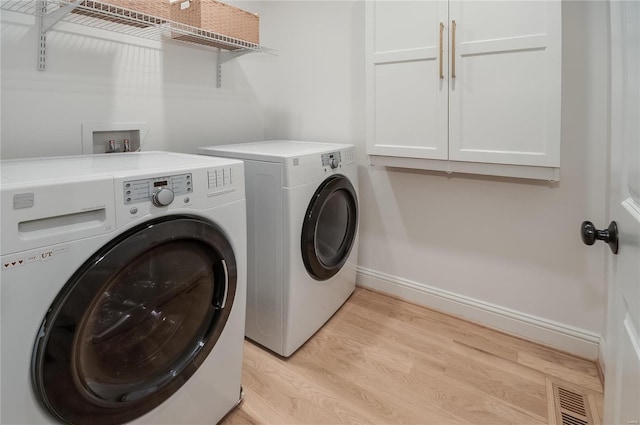 clothes washing area featuring separate washer and dryer, cabinets, and light hardwood / wood-style floors