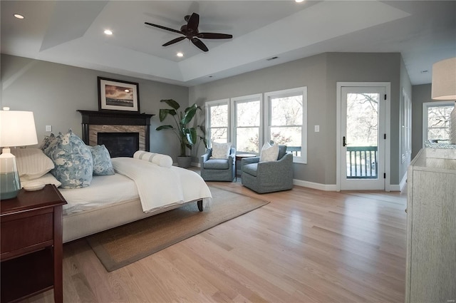 bedroom with ceiling fan, light hardwood / wood-style floors, access to exterior, and a tray ceiling