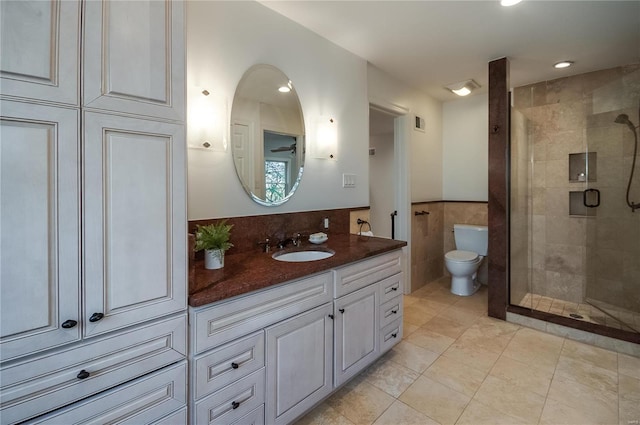 bathroom featuring tile patterned floors, vanity, a shower with door, tile walls, and toilet