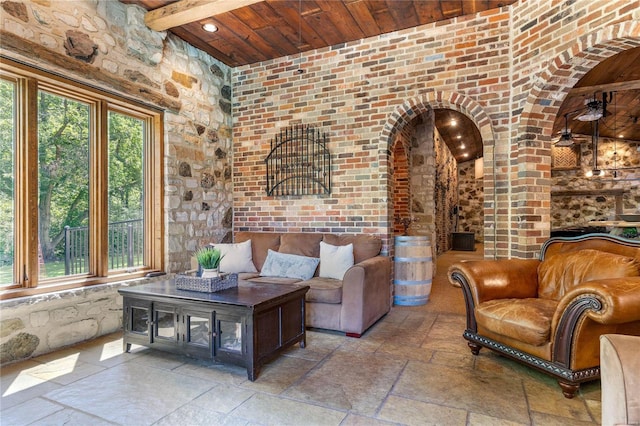 living room featuring wood ceiling, beamed ceiling, and brick wall