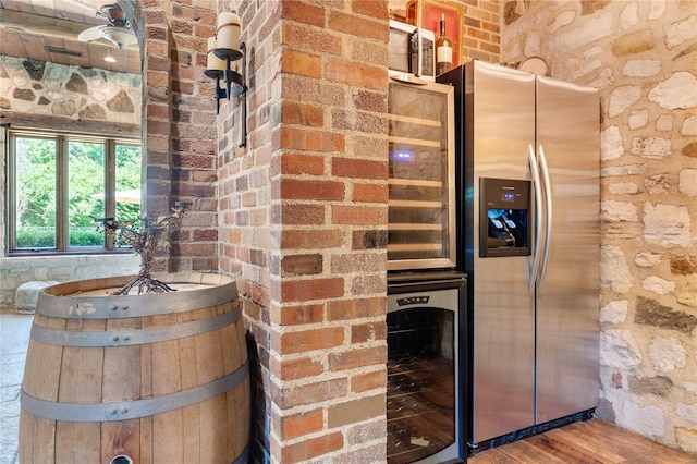 kitchen with brick wall, stainless steel refrigerator with ice dispenser, wine cooler, and hardwood / wood-style floors