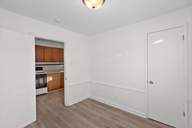 kitchen featuring decorative backsplash, sink, stainless steel stove, and light hardwood / wood-style flooring