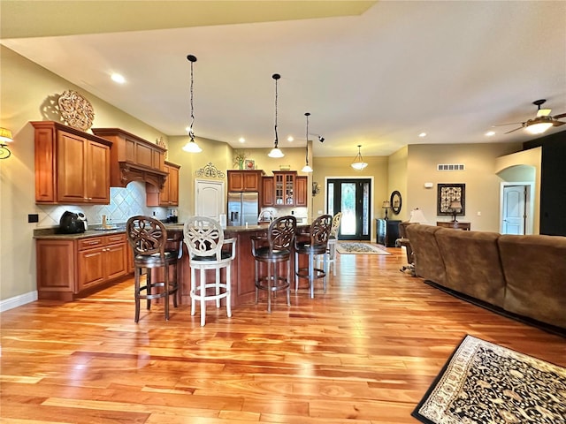 kitchen with ceiling fan, tasteful backsplash, stainless steel fridge, an island with sink, and a breakfast bar area