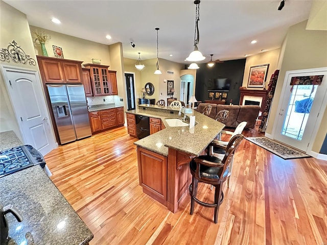 kitchen featuring a large island with sink, stainless steel fridge, decorative light fixtures, light stone counters, and a breakfast bar area