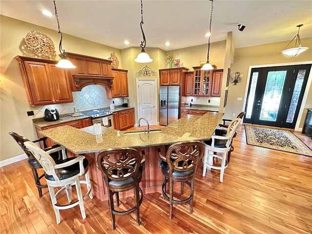 kitchen with appliances with stainless steel finishes, backsplash, sink, decorative light fixtures, and a large island