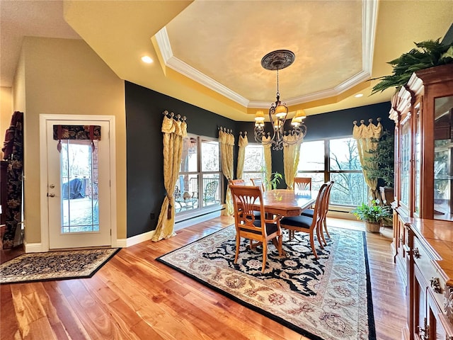 dining space with light wood-type flooring, an inviting chandelier, a raised ceiling, and plenty of natural light