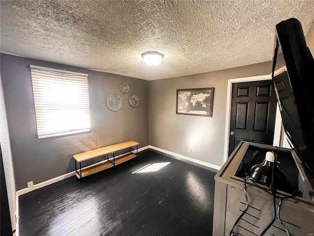 misc room with baseboards, wood finished floors, a textured ceiling, and a textured wall