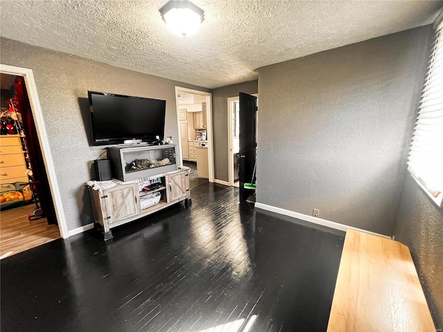 living area with a textured ceiling, a textured wall, wood finished floors, and baseboards