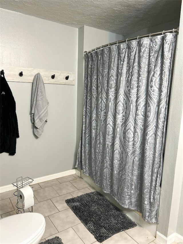 bathroom featuring baseboards, a textured ceiling, toilet, and tile patterned floors