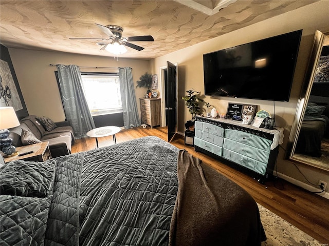 bedroom with a textured ceiling, wood finished floors, a ceiling fan, and baseboards