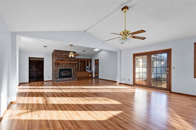 unfurnished living room featuring vaulted ceiling with beams, ceiling fan, wood-type flooring, and a brick fireplace