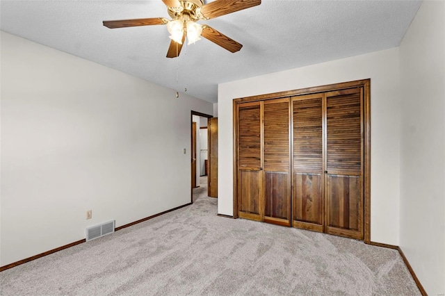 unfurnished bedroom with a textured ceiling, a closet, ceiling fan, and light colored carpet