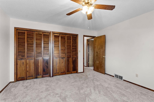 unfurnished bedroom with a textured ceiling, light colored carpet, ceiling fan, and multiple closets