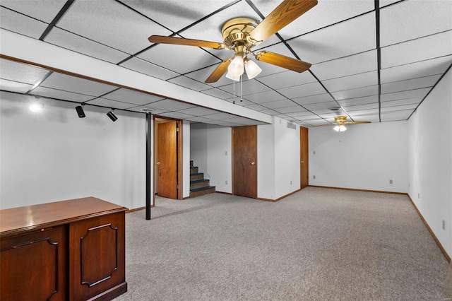 basement with a paneled ceiling, ceiling fan, and light colored carpet