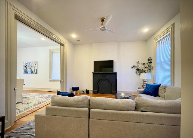 living room featuring ceiling fan, light wood-type flooring, and a fireplace