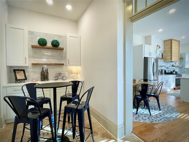 bar with white cabinets, light wood-type flooring, stainless steel appliances, and tasteful backsplash