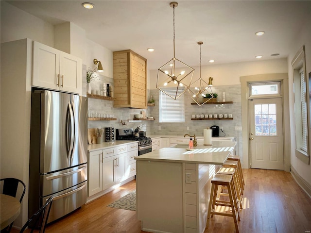 kitchen with stainless steel appliances, an island with sink, a breakfast bar, white cabinets, and light wood-type flooring