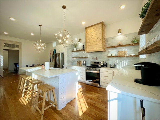 kitchen with white cabinetry, stainless steel appliances, light hardwood / wood-style flooring, backsplash, and a kitchen bar