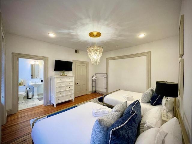 bedroom with wood-type flooring, connected bathroom, and an inviting chandelier