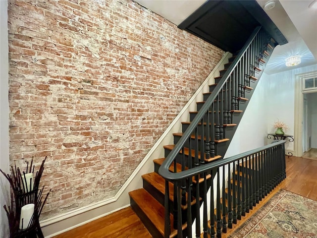 stairway with wood-type flooring and brick wall