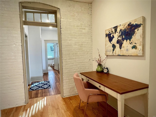 home office featuring wood-type flooring and brick wall