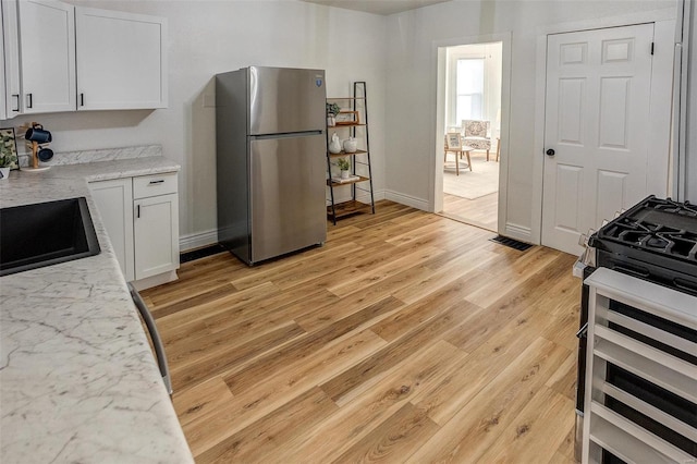 kitchen with stainless steel refrigerator, stove, white cabinets, and light wood-type flooring