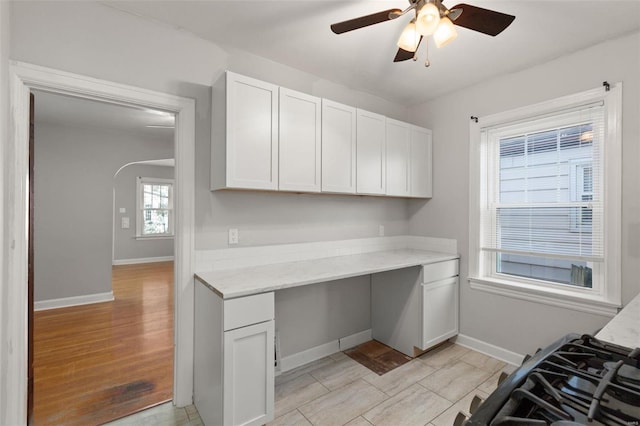 kitchen featuring light stone countertops, ceiling fan, built in desk, white cabinets, and light hardwood / wood-style floors