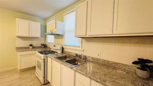 kitchen with sink, white range with gas stovetop, white cabinets, light stone countertops, and backsplash