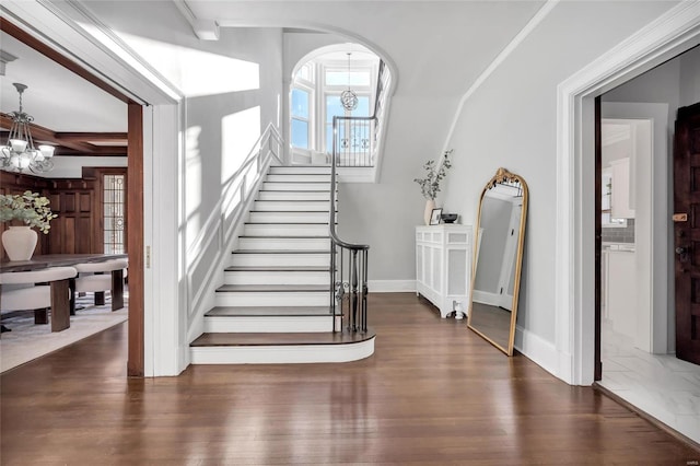 stairs featuring hardwood / wood-style floors, ornamental molding, beamed ceiling, and an inviting chandelier