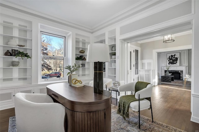 office space featuring built in shelves, crown molding, dark wood-type flooring, an inviting chandelier, and a fireplace