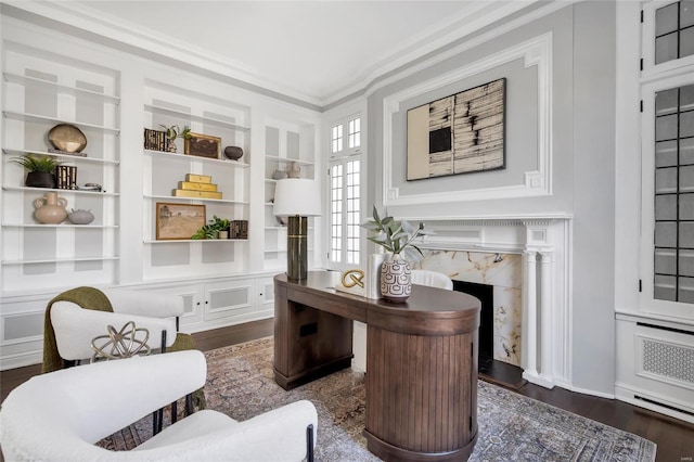 living area with a high end fireplace, built in shelves, ornamental molding, and dark wood-type flooring