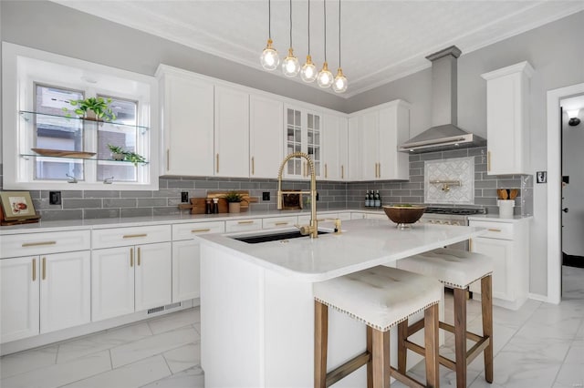 kitchen featuring white cabinetry, a center island with sink, wall chimney range hood, and sink