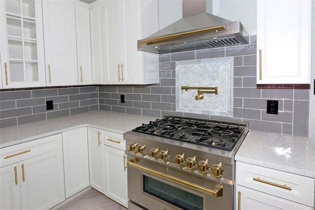 kitchen featuring light stone countertops, tasteful backsplash, high end stainless steel range oven, wall chimney range hood, and white cabinetry