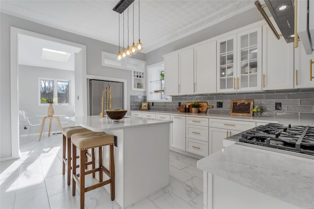 kitchen with white cabinetry, light stone counters, backsplash, decorative light fixtures, and a kitchen island