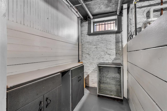 interior space featuring wine cooler, wood walls, and concrete floors