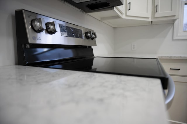 kitchen with light stone countertops, electric range, and white cabinetry